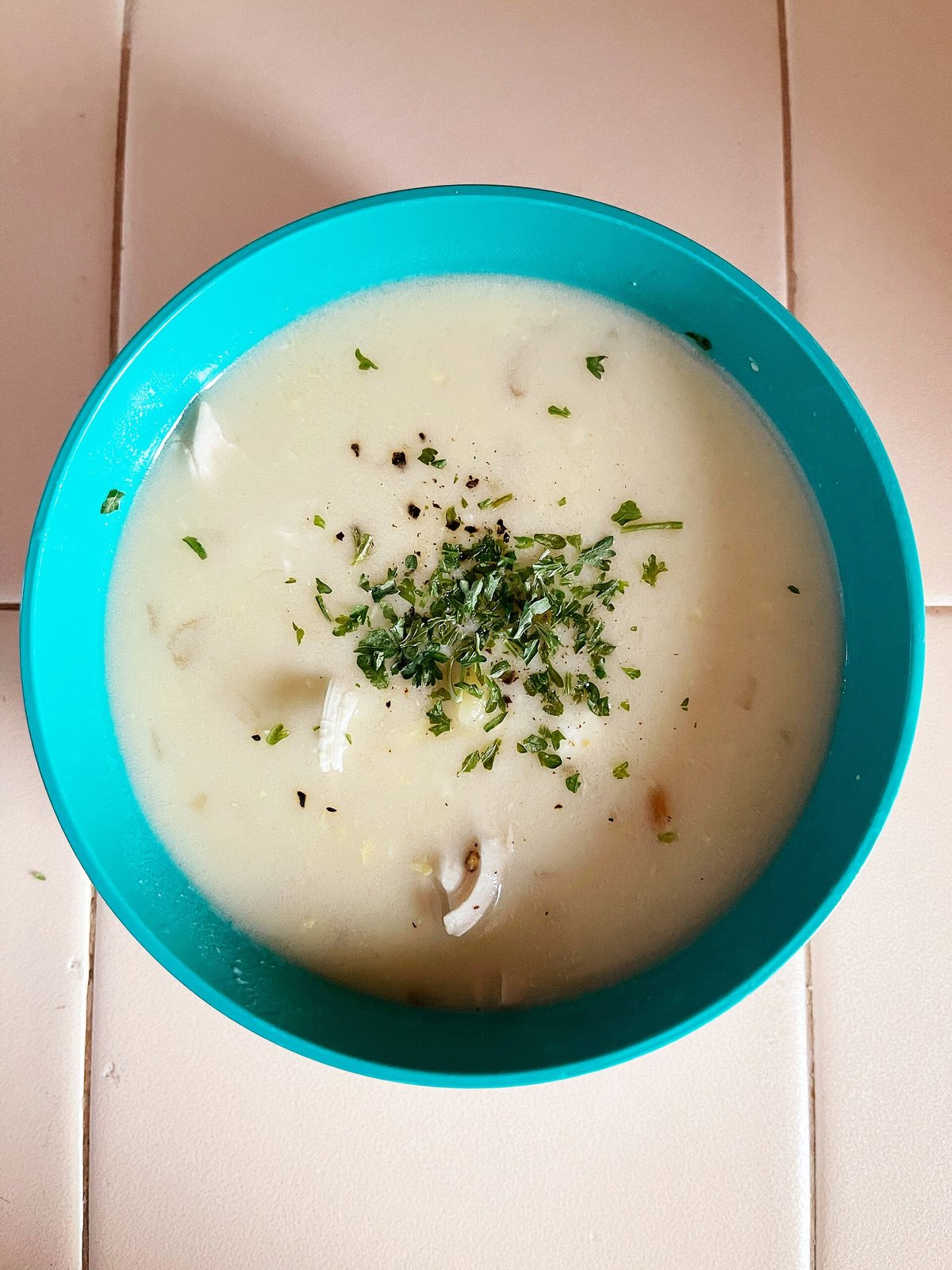 A bowl of pale golden avgolemono soup with shredded chicken, rice and a lemon wedge