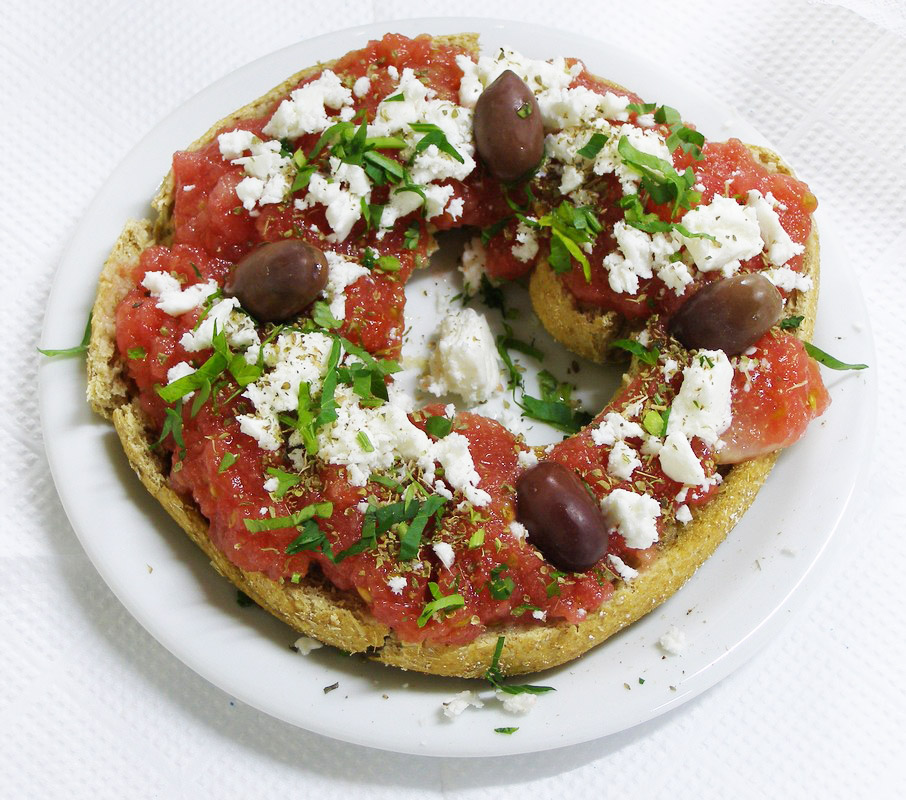 A barley rusk topped with grated tomato, crumbled white cheese, olives and oregano