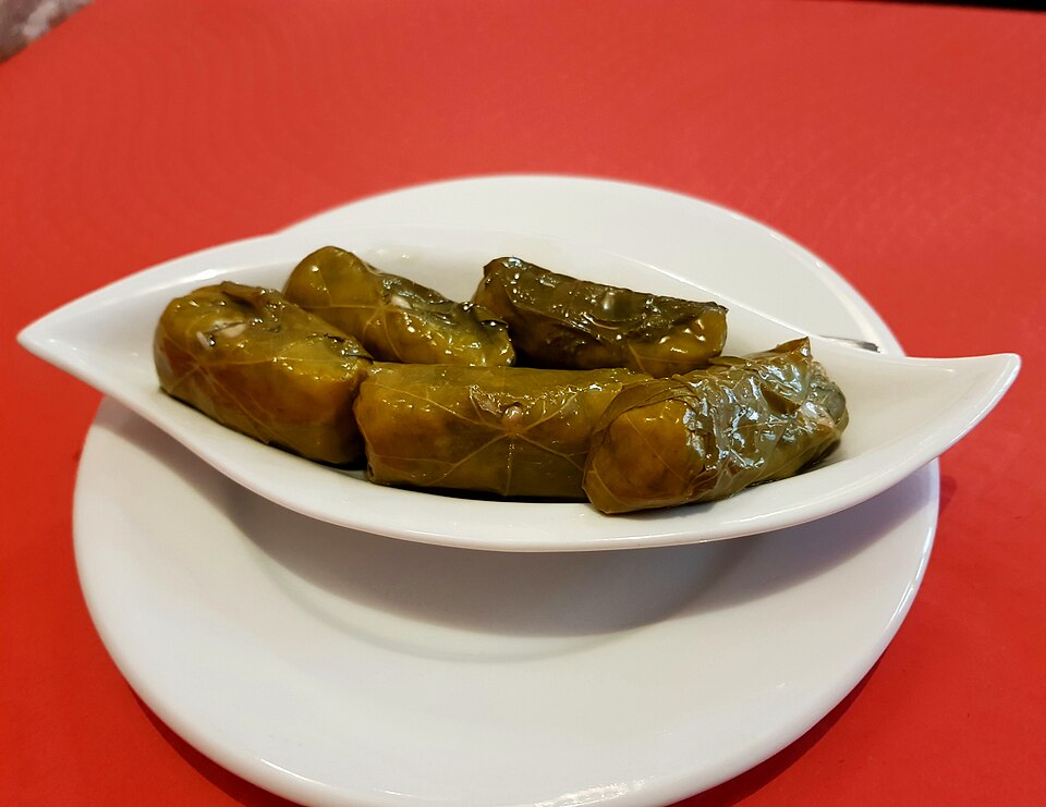 Rolled stuffed vine leaves arranged in a dish with lemon wedges and olive oil