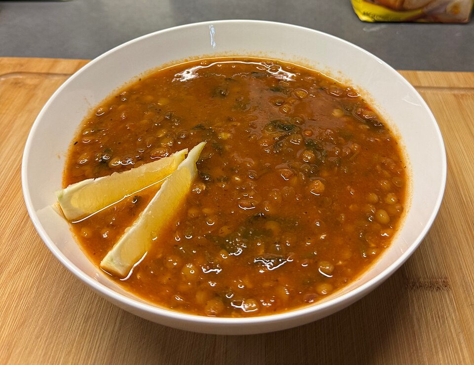 A bowl of thick Greek lentil soup with olive oil and a small jug of vinegar