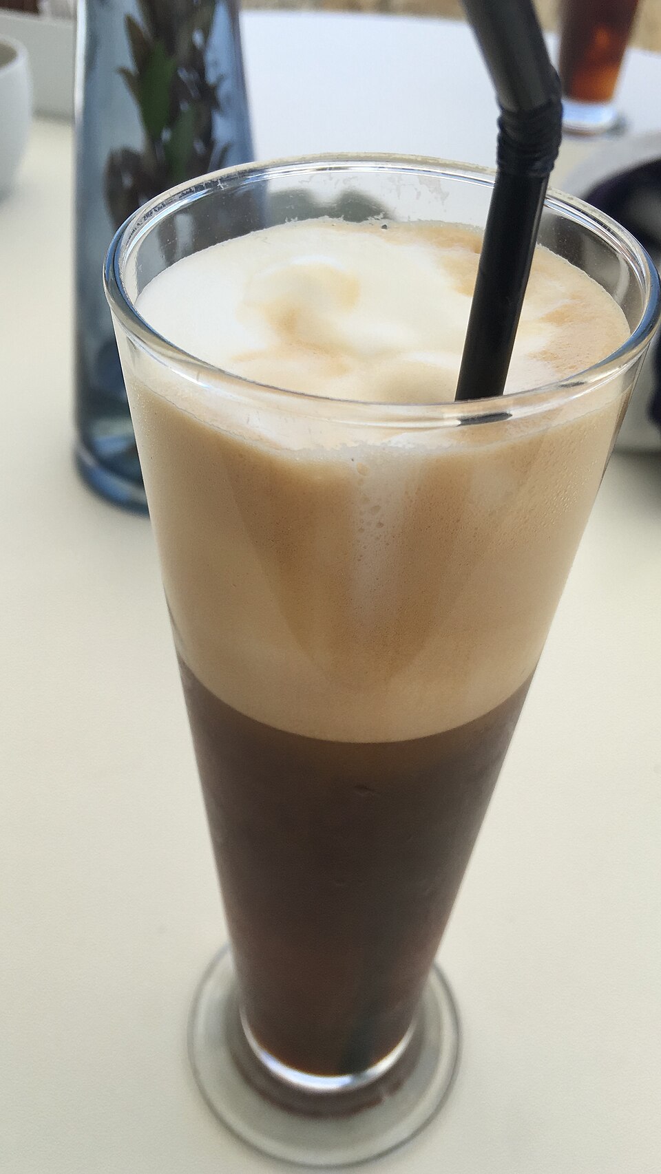 A tall glass of Greek frappe iced coffee with a thick foam head
