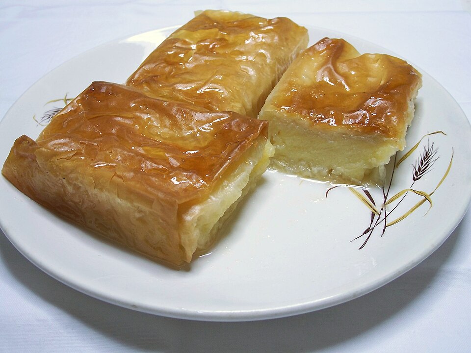 A square of galaktoboureko showing thick yellow custard between crisp golden phyllo