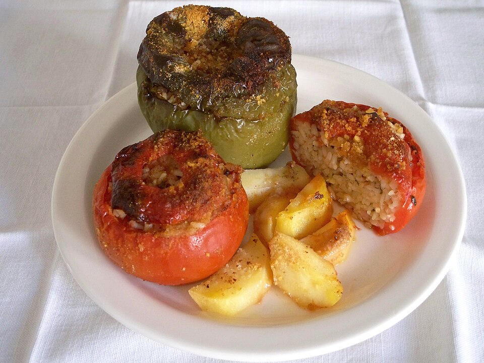 A tray of baked stuffed tomatoes and peppers with browned tops and potato wedges between them