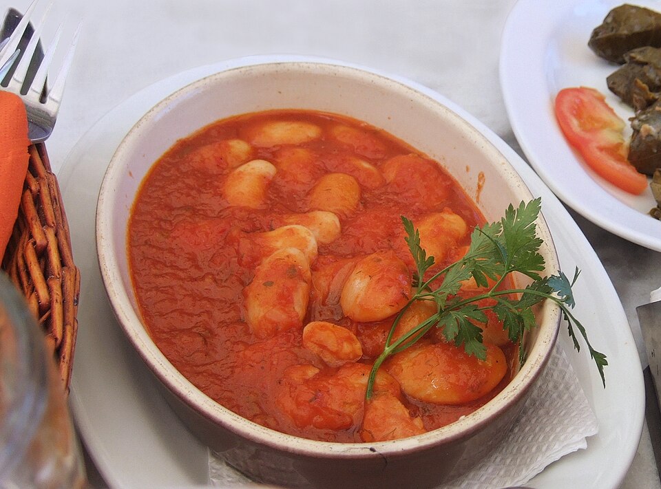 A dish of baked giant beans in a rich orange tomato sauce with parsley and olive oil