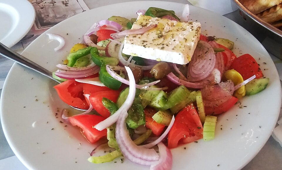 A Greek village salad with tomato wedges, cucumber, red onion and a whole slab of feta topped with oregano