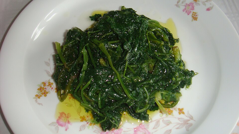 A plate of dark boiled greens dressed with olive oil and lemon wedges