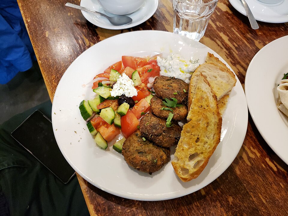 Golden Greek courgette fritters piled on a plate with tzatziki and lemon