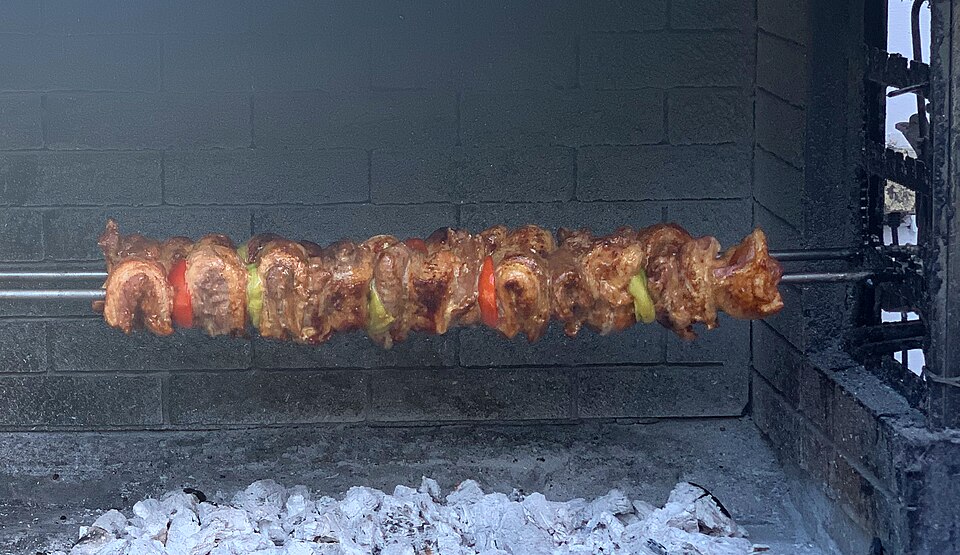 Kontosouvli pork chunks slow-turning on a spit over charcoal