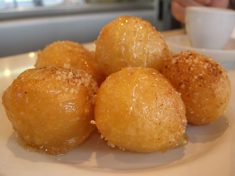 A bowl of golden loukoumades glossy with honey, dusted with cinnamon and chopped walnuts