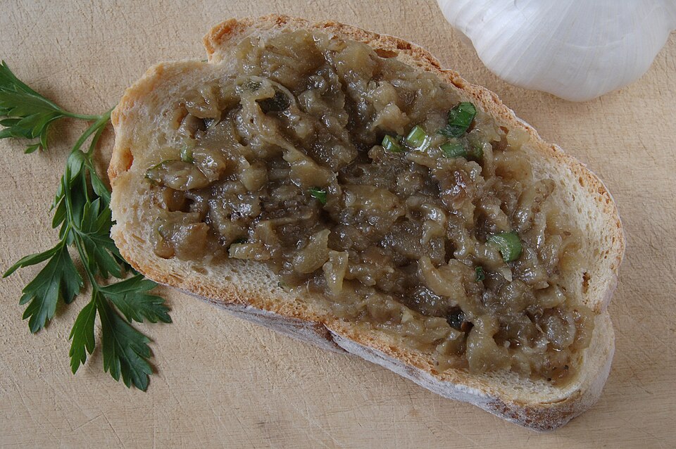 A bowl of rough-textured aubergine dip with olive oil, parsley and a scattering of walnuts