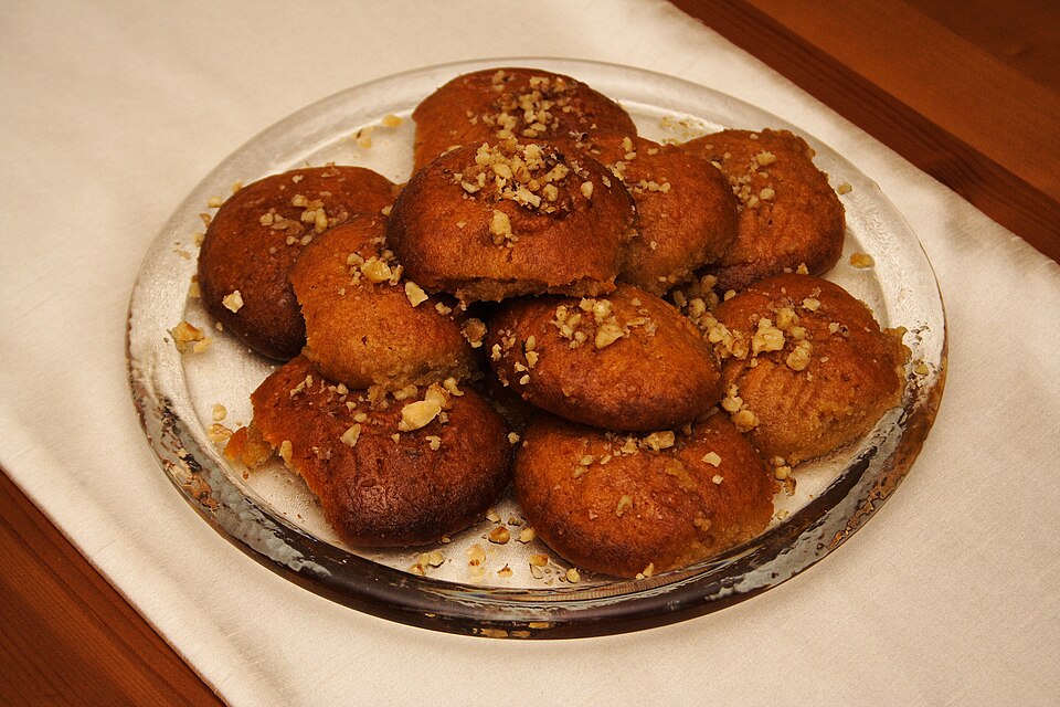 Oval honey-soaked Greek Christmas cookies topped with chopped walnuts