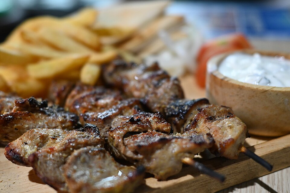 Charred pork souvlaki skewers on a wooden board with lemon wedges and oregano