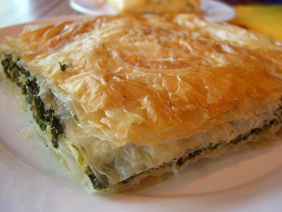 A tray of spanakopita cut into squares showing green spinach filling under crisp golden phyllo