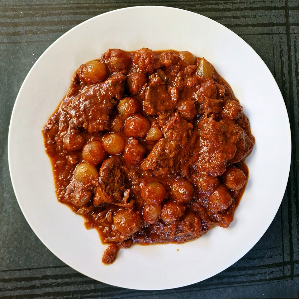 A pot of Greek beef stifado with whole small onions in a dark cinnamon-spiced sauce