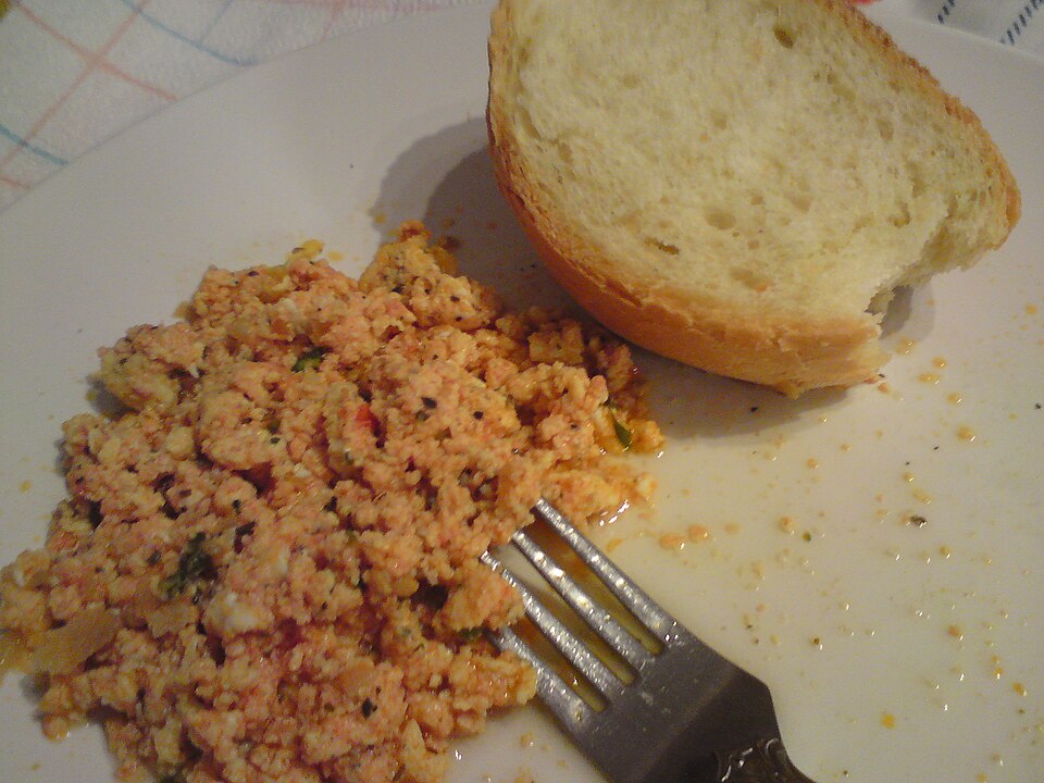 Greek scrambled eggs with tomato and crumbled feta in a pan with bread