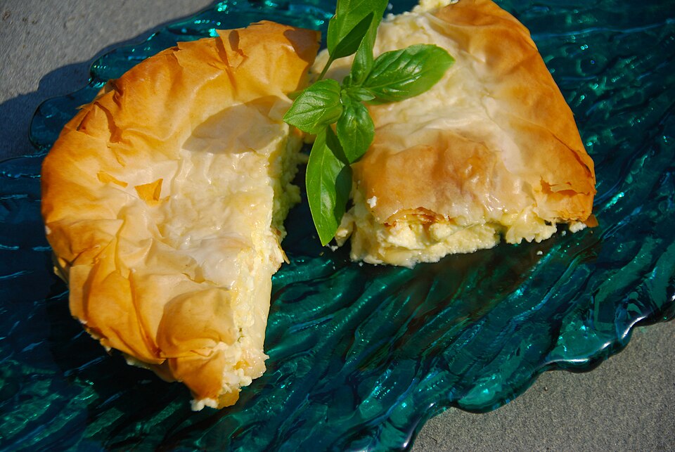 A square of Greek cheese pie with crisp layered phyllo and a pale creamy filling