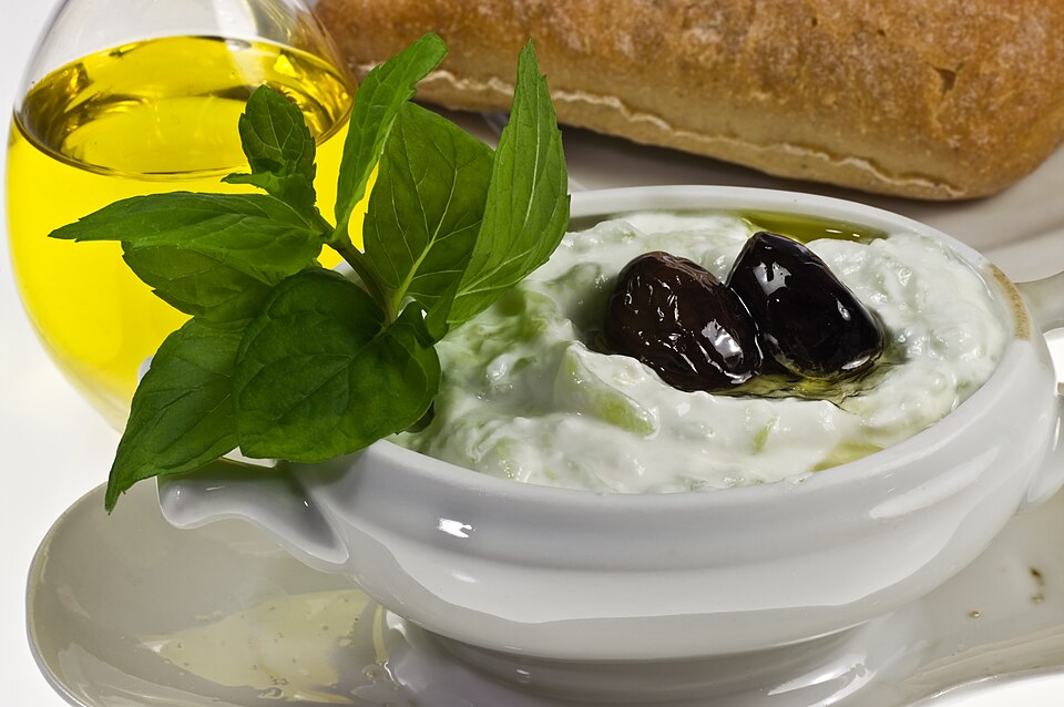 A bowl of thick white tzatziki with olive oil pooled on top and a sprig of dill